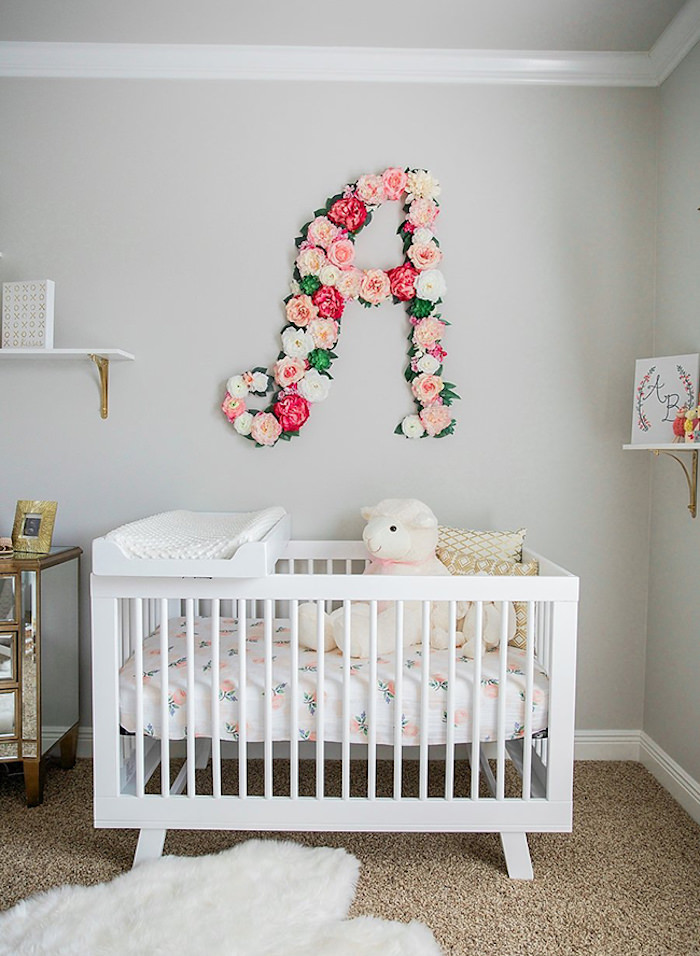 دکوراسیون اتاق خواب نوزاد با دیوارهای خاکستری و تخت نوزاد سفید که به زیبایی با دسته گل a شکل تزیین شده است